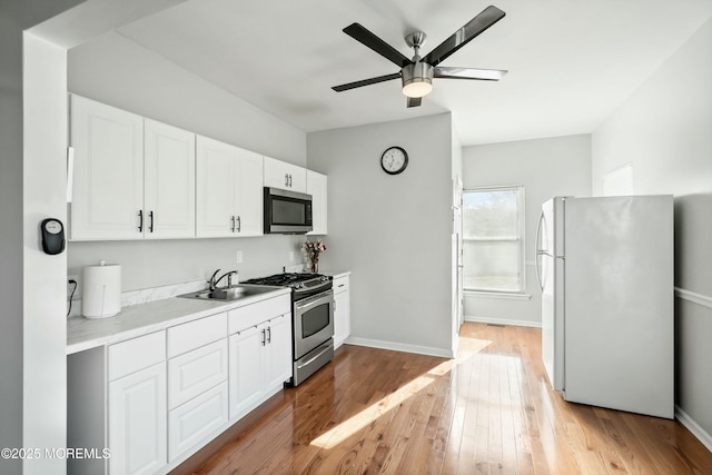 kitchen featuring light wood-type flooring, stainless steel appliances, ceiling fan, sink, and white cabinets