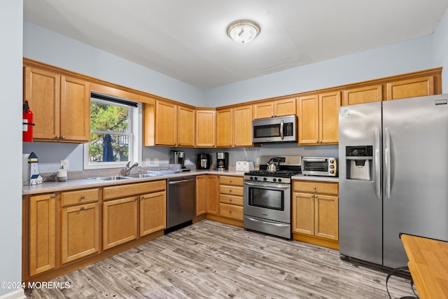 kitchen with appliances with stainless steel finishes, light hardwood / wood-style flooring, and sink