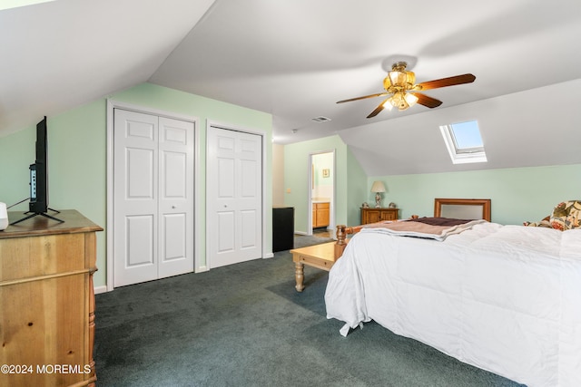 carpeted bedroom featuring ceiling fan, vaulted ceiling with skylight, and two closets