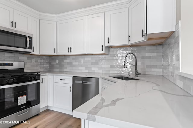 kitchen featuring light stone countertops, white cabinetry, sink, stainless steel appliances, and tasteful backsplash