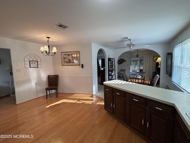 kitchen with dark brown cabinetry, ceiling fan with notable chandelier, light hardwood / wood-style floors, and decorative light fixtures