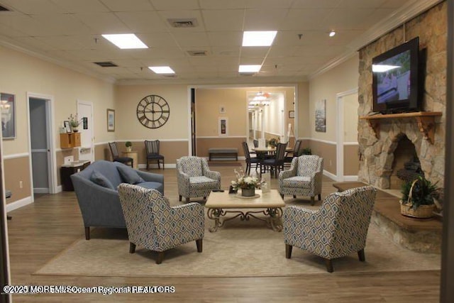 living room with wood-type flooring, a paneled ceiling, a stone fireplace, and crown molding