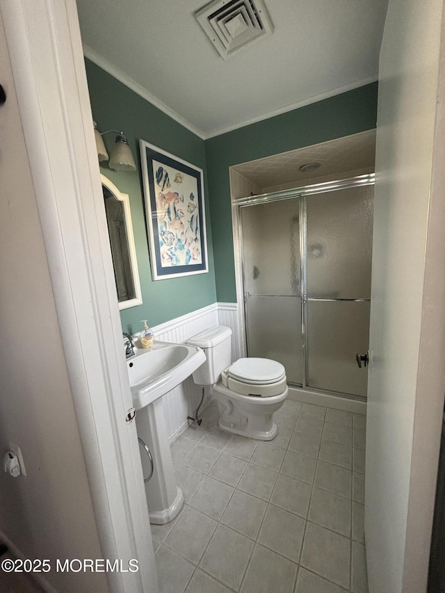 bathroom featuring toilet, tile patterned flooring, a shower with shower door, and ornamental molding