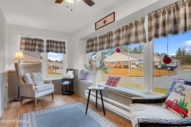 living area featuring ceiling fan, wood walls, wood-type flooring, and a baseboard heating unit