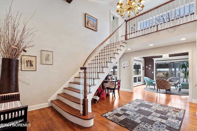 stairs featuring wood-type flooring, high vaulted ceiling, and an inviting chandelier