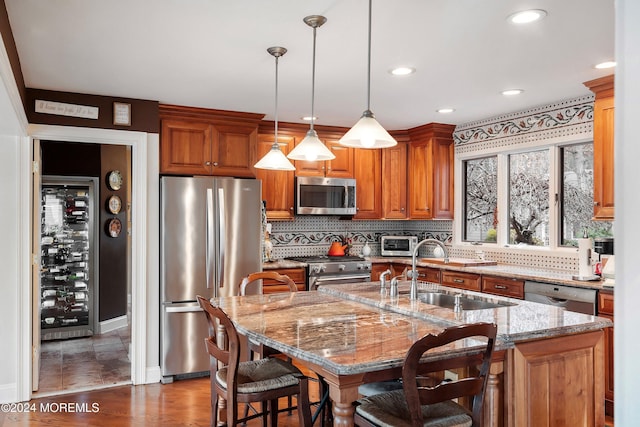 kitchen with sink, stainless steel appliances, dark hardwood / wood-style flooring, decorative light fixtures, and a center island with sink