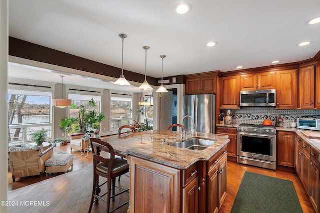 kitchen with sink, light hardwood / wood-style floors, a kitchen bar, a kitchen island with sink, and appliances with stainless steel finishes