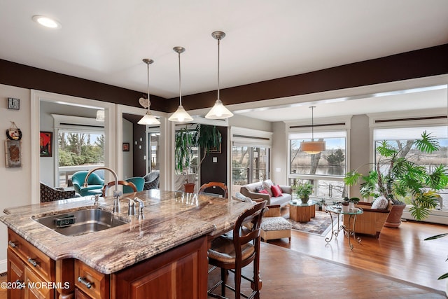 kitchen featuring a breakfast bar, sink, light stone countertops, decorative light fixtures, and wood-type flooring