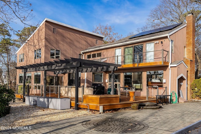 rear view of house featuring a sunroom, solar panels, a pergola, a balcony, and a wooden deck