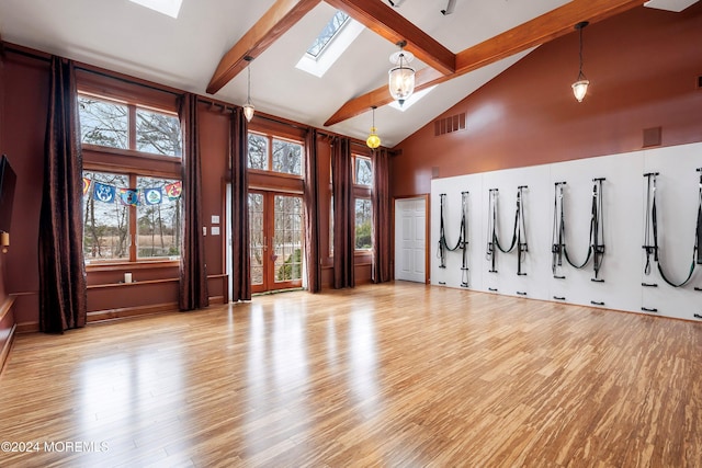 interior space with beam ceiling, a skylight, light hardwood / wood-style flooring, and high vaulted ceiling