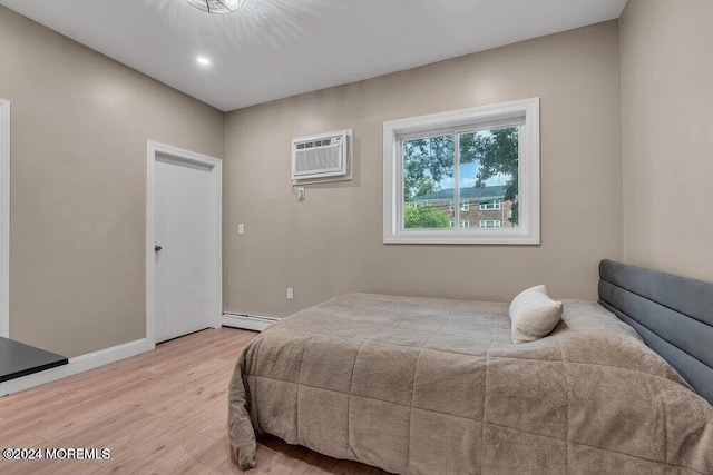 bedroom featuring a wall unit AC, light hardwood / wood-style flooring, and a baseboard radiator