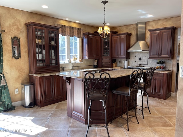 kitchen with a breakfast bar, wall chimney range hood, pendant lighting, a notable chandelier, and a center island