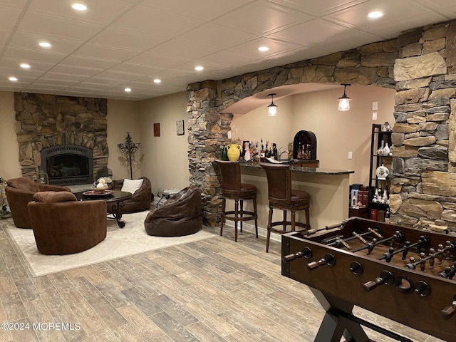 game room with light wood-type flooring, a stone fireplace, and bar