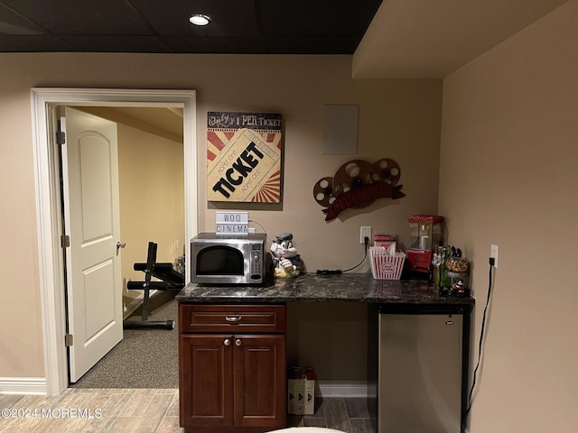 bar featuring refrigerator, dark brown cabinetry, and dark stone counters