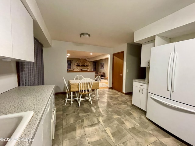 kitchen with white refrigerator, light stone countertops, white cabinetry, and sink