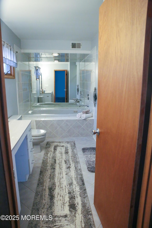 bathroom with tile patterned floors, vanity, toilet, and tiled bath