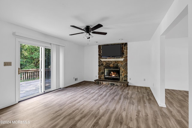 unfurnished living room with light hardwood / wood-style floors, a stone fireplace, and ceiling fan