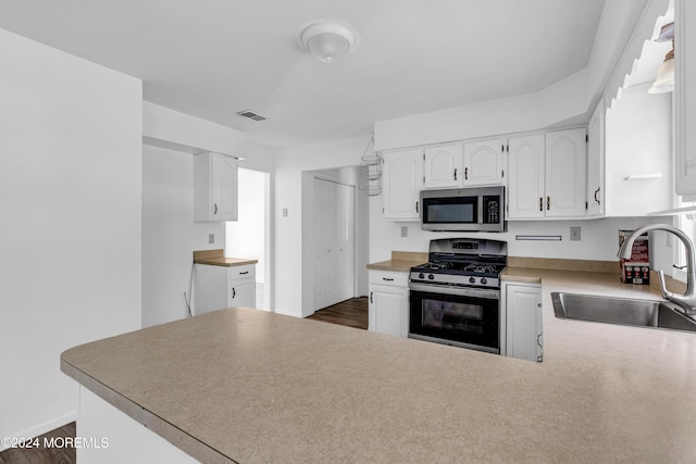 kitchen with sink, kitchen peninsula, dark hardwood / wood-style floors, appliances with stainless steel finishes, and white cabinetry