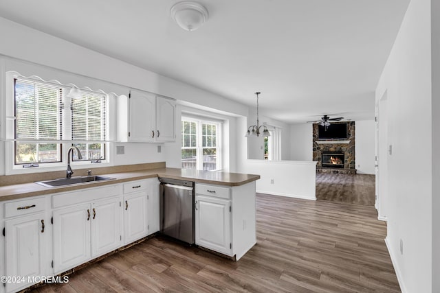 kitchen with white cabinetry, dishwasher, sink, a stone fireplace, and kitchen peninsula