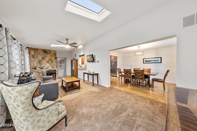 living room featuring a stone fireplace, carpet floors, a skylight, and ceiling fan with notable chandelier