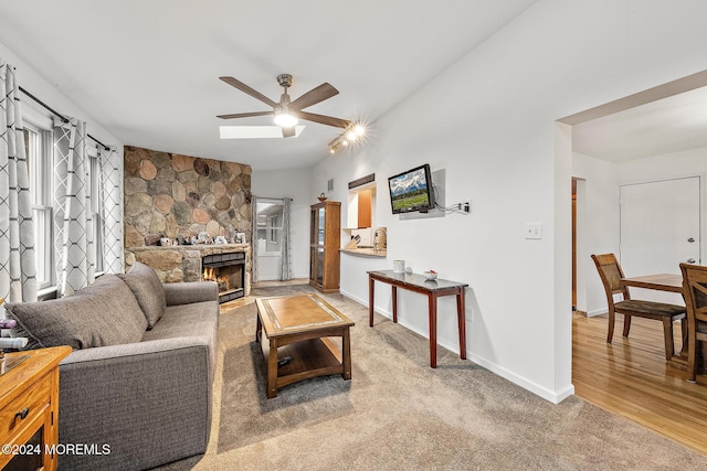 living room with ceiling fan, a stone fireplace, and carpet floors