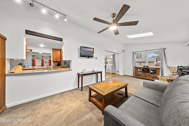 carpeted living room featuring rail lighting, lofted ceiling with skylight, and ceiling fan