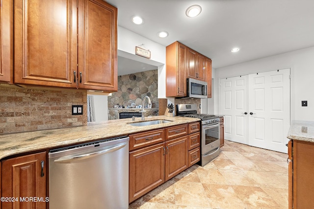 kitchen with backsplash, light stone counters, sink, and appliances with stainless steel finishes