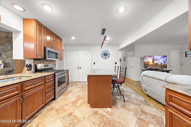 kitchen featuring sink, stainless steel appliances, light stone counters, a breakfast bar, and a kitchen island