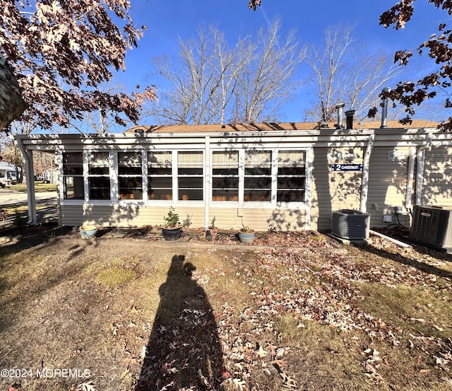 rear view of house with central air condition unit and a sunroom