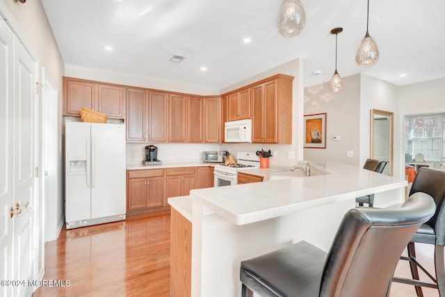 kitchen with kitchen peninsula, light wood-type flooring, white appliances, pendant lighting, and a breakfast bar area