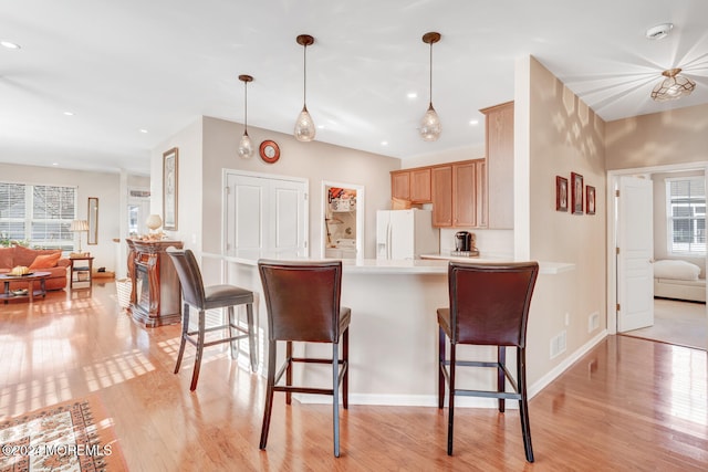 kitchen featuring light hardwood / wood-style flooring, white refrigerator with ice dispenser, kitchen peninsula, decorative light fixtures, and light brown cabinetry