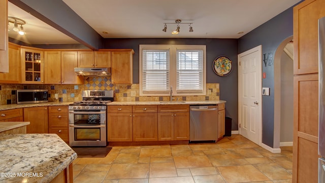 kitchen featuring decorative backsplash, stainless steel appliances, light stone countertops, and sink