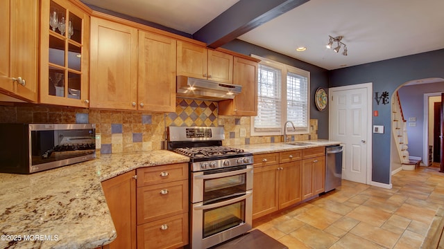 kitchen with decorative backsplash, appliances with stainless steel finishes, light stone countertops, sink, and beam ceiling