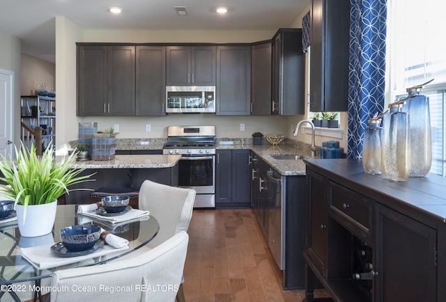 kitchen featuring dark wood-type flooring, sink, light stone counters, dark brown cabinetry, and stainless steel appliances