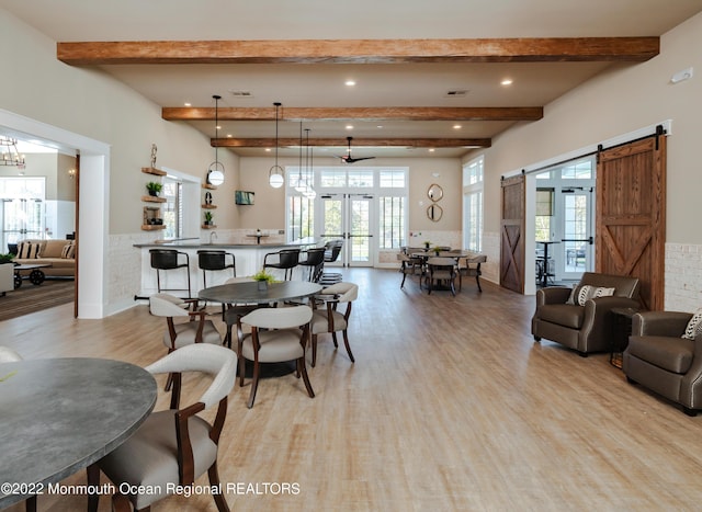 dining room featuring beamed ceiling, a barn door, light wood-type flooring, and french doors