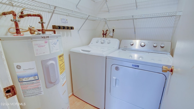 clothes washing area with electric water heater, washer and dryer, and light wood-type flooring