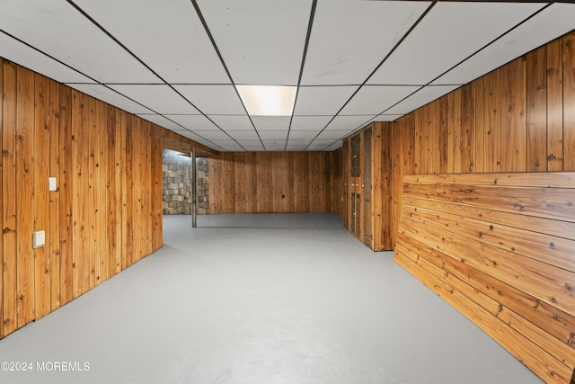 basement with a drop ceiling and wood walls