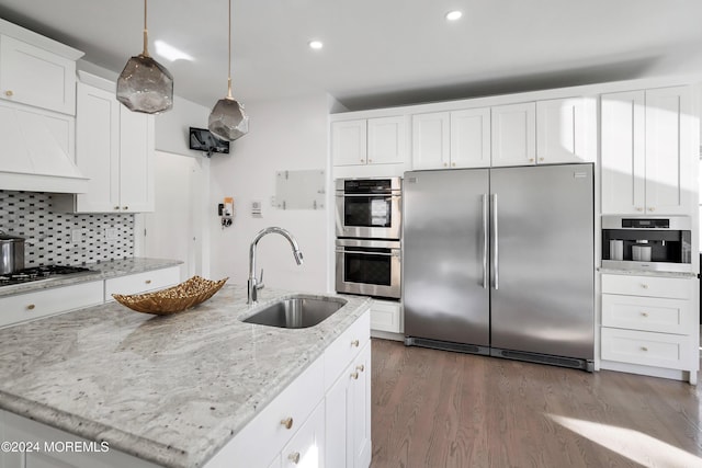 kitchen featuring a center island with sink, sink, decorative backsplash, light wood-type flooring, and appliances with stainless steel finishes