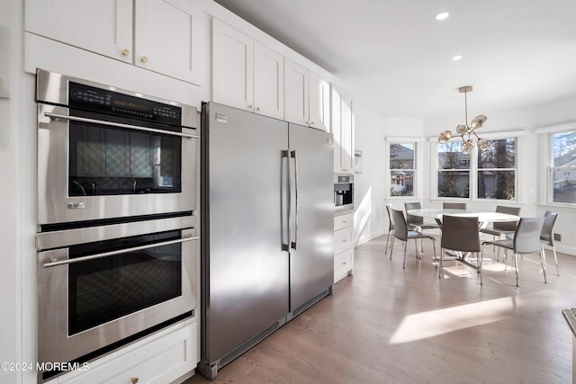 kitchen with light wood-type flooring, decorative light fixtures, white cabinetry, stainless steel appliances, and a chandelier