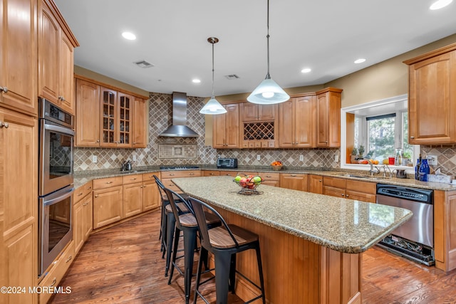 kitchen featuring light stone countertops, a center island, sink, wall chimney range hood, and appliances with stainless steel finishes