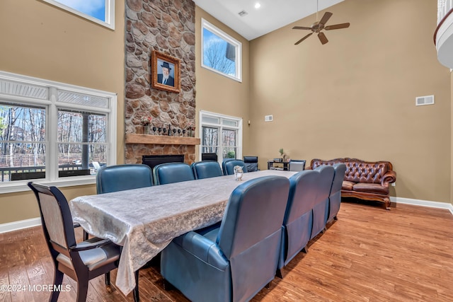 dining space featuring a stone fireplace, ceiling fan, light hardwood / wood-style flooring, and a high ceiling