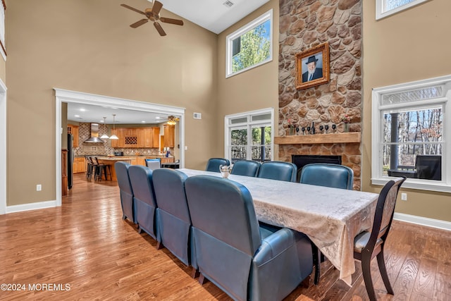 dining room featuring a stone fireplace, high vaulted ceiling, and light hardwood / wood-style floors