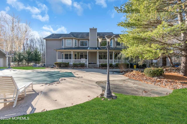 rear view of property with a lawn, a patio, and a covered pool