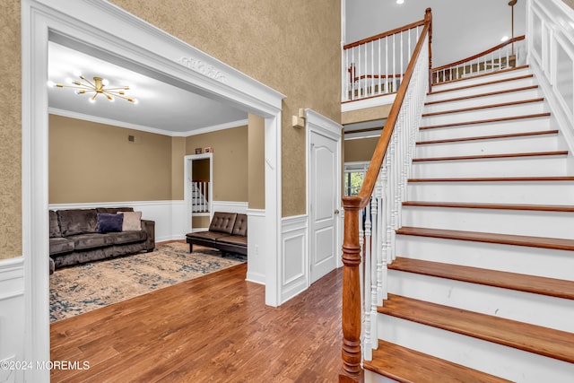 staircase featuring wood-type flooring, crown molding, and an inviting chandelier