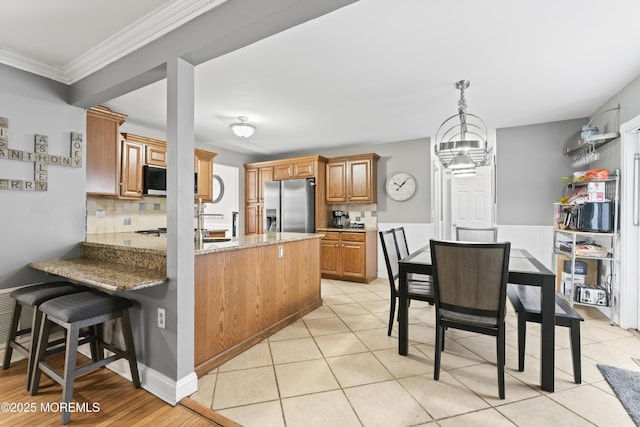 kitchen with stainless steel fridge, light stone counters, a notable chandelier, tasteful backsplash, and kitchen peninsula