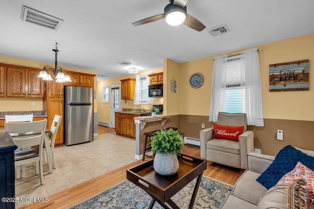 living room with ceiling fan with notable chandelier, baseboard heating, and light wood-type flooring