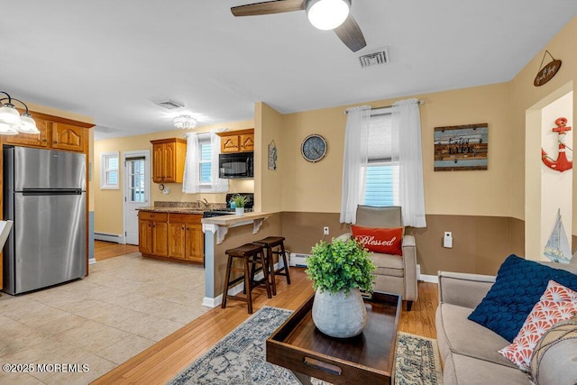 living room with light hardwood / wood-style floors, baseboard heating, and ceiling fan