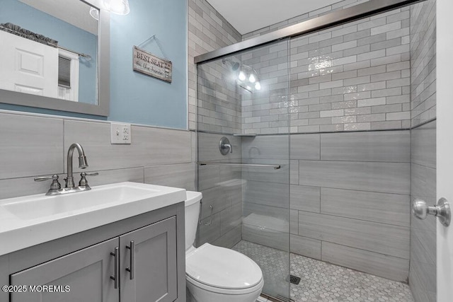 bathroom with vanity, toilet, tile walls, and a shower with shower door