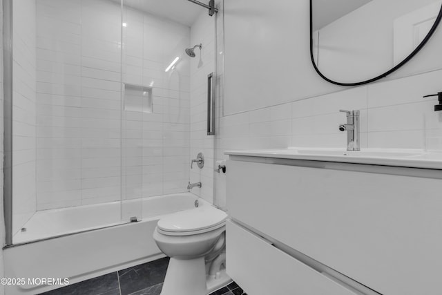 full bathroom with tile patterned flooring, enclosed tub / shower combo, toilet, vanity, and tile walls