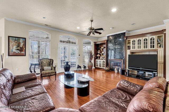 living room featuring ceiling fan, a premium fireplace, crown molding, wood-type flooring, and a textured ceiling